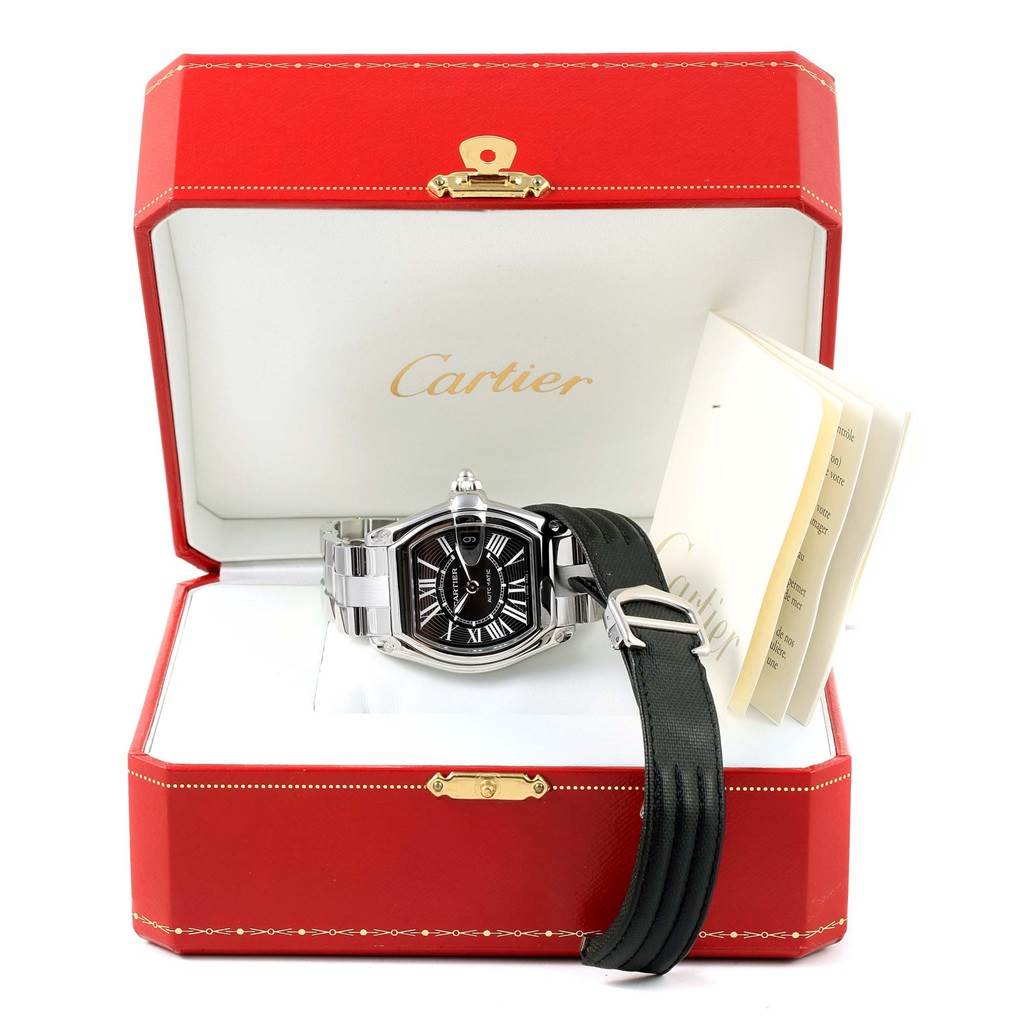 The image shows a Cartier Roadster W62041V3 Men
s Stainless Steel Black Dial W62041V3 Men
s Stainless Steel Black Dial model watch in its original box, displayed with an additional strap and accompanying documents.
