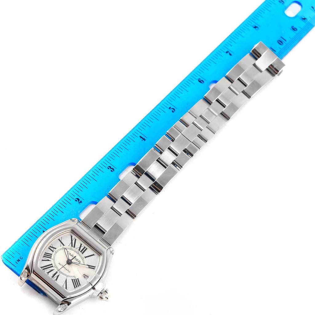 The image shows the Cartier Roadster W62025V3 Men's Stainless Steel Silver Dial W62025V3 Men's Stainless Steel Silver Dial watch laid flat with its strap extended alongside a blue ruler.