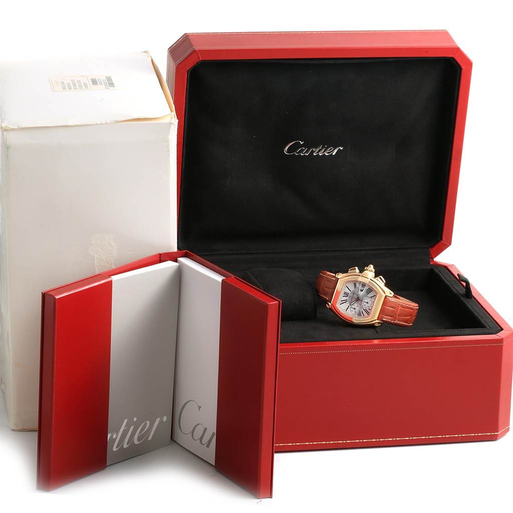 The Cartier Roadster W62021Y2 Men's Yellow Gold Silver Dial W62021Y2 Men's Yellow Gold Silver Dial watch is displayed in its red box, alongside a red and white booklet, with the box lid open at a slight angle.