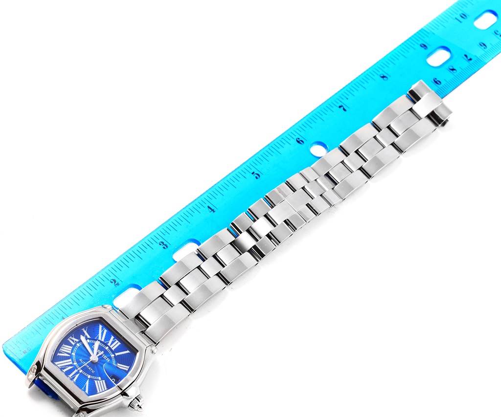 The image shows the face and metal band of a Cartier Roadster W62048V3 Men's Stainless Steel Blue Dial W62048V3 Men's Stainless Steel Blue Dial watch next to a blue ruler, at a top-down angle.