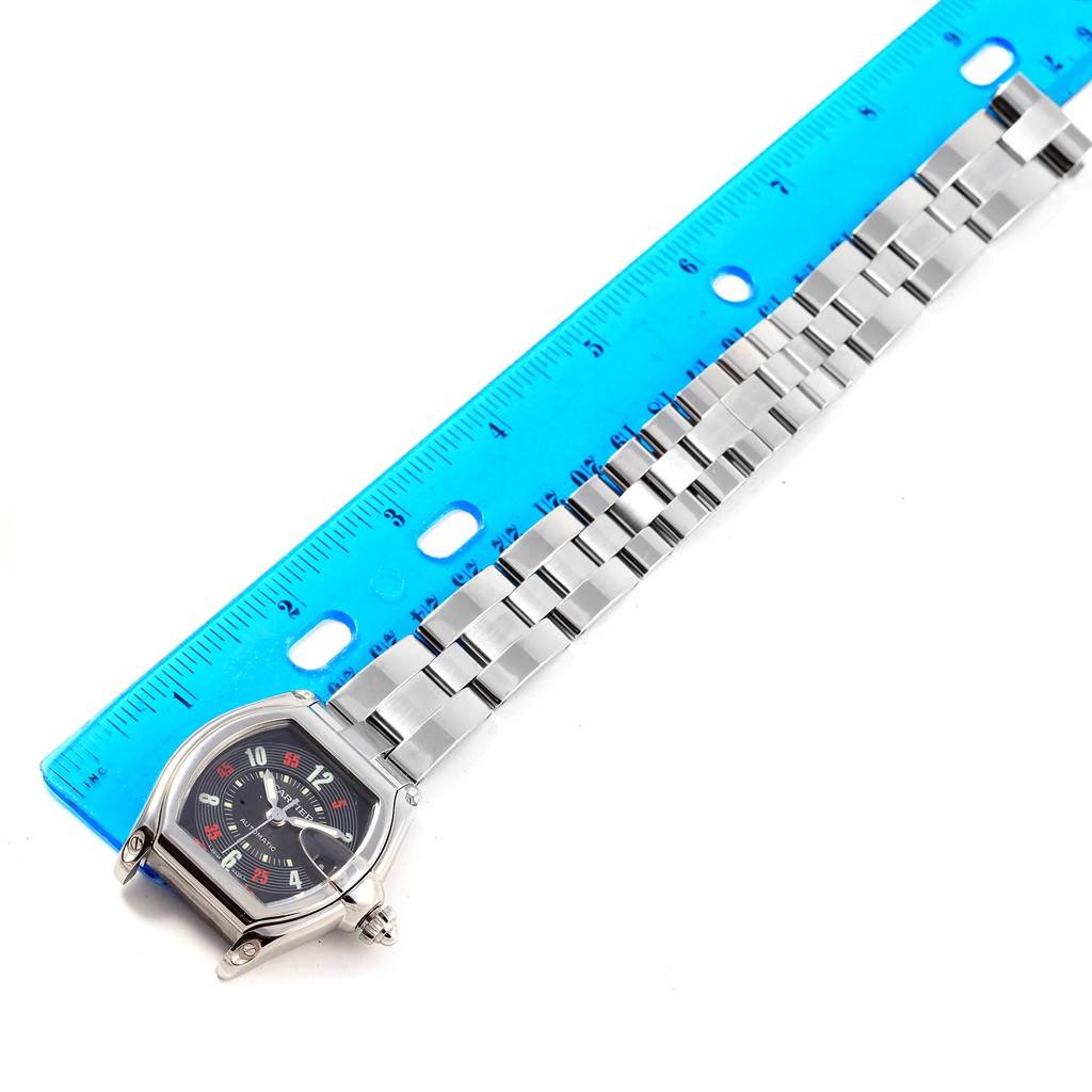 The Cartier Roadster W62002V3 Men's Stainless Steel Black Dial W62002V3 Men's Stainless Steel Black Dial watch is shown at an overhead angle, highlighting its face and metal bracelet next to a blue ruler for scale.