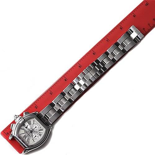 The Cartier Roadster W62019X6 Men's Stainless Steel Silver Dial W62019X6 Men's Stainless Steel Silver Dial watch is shown from an angled top-down view, displaying the face and full metallic band placed beside a ruler.