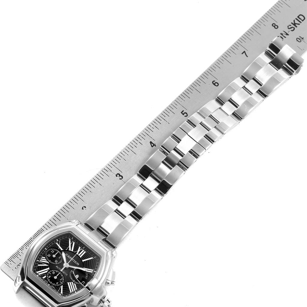 The image shows a Cartier Roadster W62020X6 Men's Stainless Steel Black Dial W62020X6 Men's Stainless Steel Black Dial model watch placed beside a ruler, displaying the watch's face and the metal bracelet.