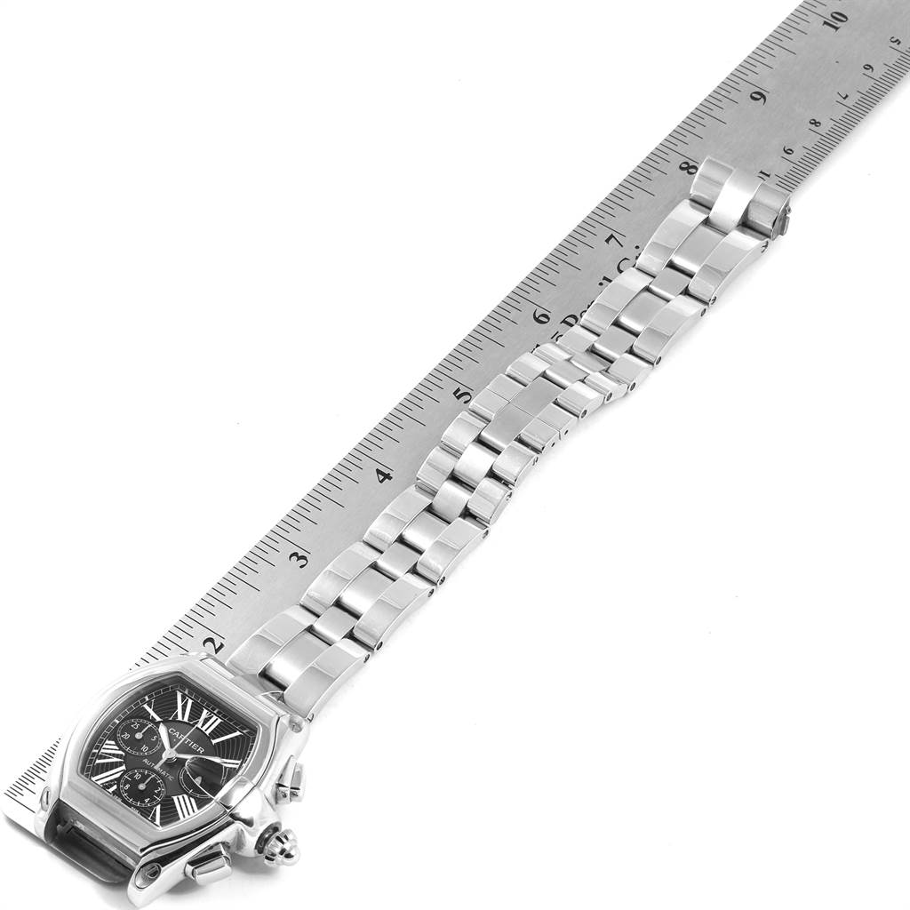 The image shows a Cartier Roadster W62020X6 Men's Stainless Steel Black Dial W62020X6 Men's Stainless Steel Black Dial watch laid flat alongside a ruler, highlighting the watch face and bracelet.