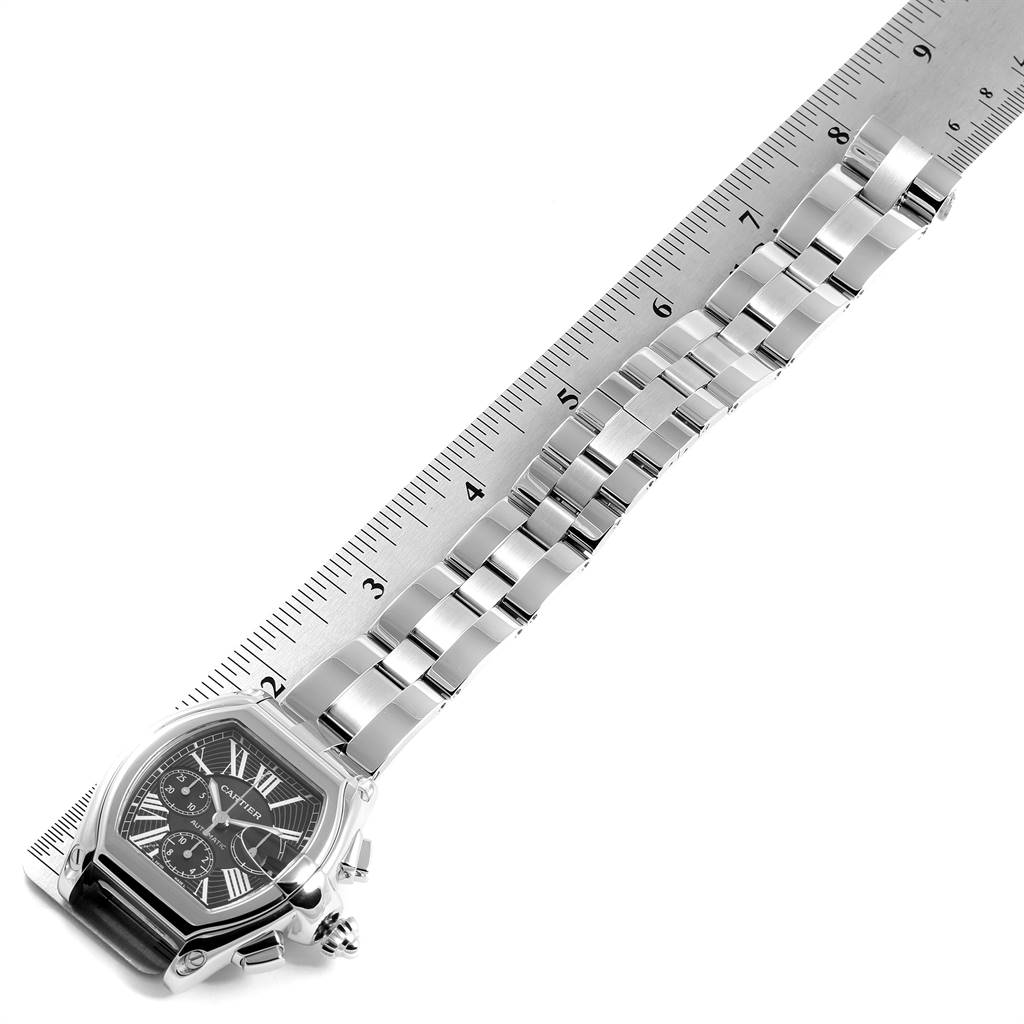 The image shows a Cartier Roadster W62020X6 Men
s Stainless Steel Black Dial W62020X6 Men
s Stainless Steel Black Dial watch laid out with its metal bracelet alongside a ruler for size reference.