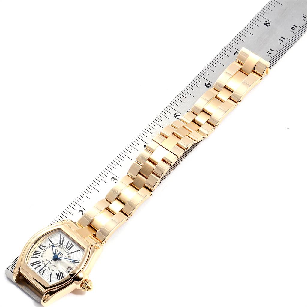 The Cartier Roadster W62005V1 Men's Yellow Gold Silver Dial W62005V1 Men's Yellow Gold Silver Dial watch is shown at an angle, highlighting the face, bracelet, and a ruler for measurement.