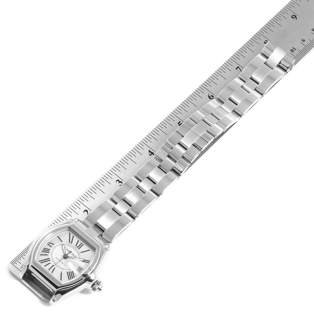 The image shows a Cartier Roadster W62025V3 Men
s Stainless Steel Silver Dial W62025V3 Men
s Stainless Steel Silver Dial watch laid next to a ruler, showcasing its face and metal bracelet.