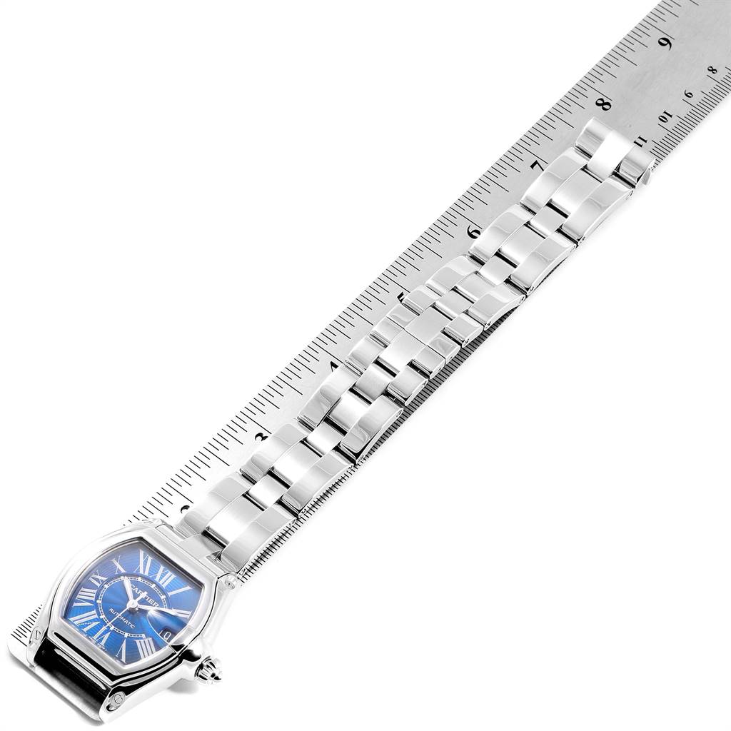 This image shows the Cartier Roadster W62048V3 Men's Stainless Steel Blue Dial W62048V3 Men's Stainless Steel Blue Dial watch laid flat next to a ruler, highlighting its face and bracelet.