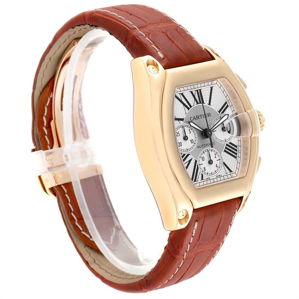 The image shows a Cartier Roadster W62021Y3 Men's Yellow Gold Silver Dial W62021Y3 Men's Yellow Gold Silver Dial watch at an angle highlighting its brown leather strap and silver dial with Roman numerals.