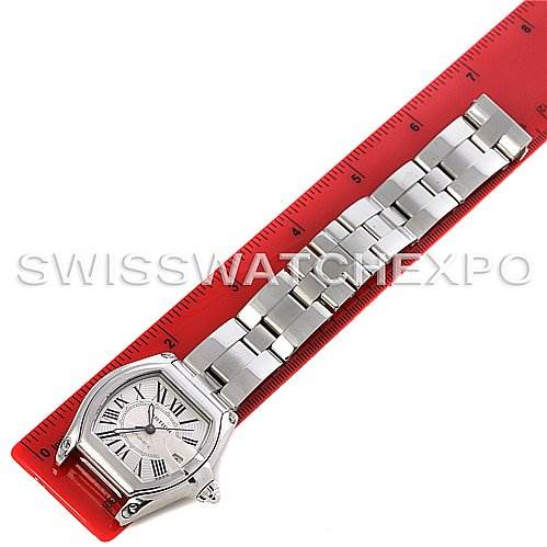 The image shows a Cartier Roadster W62025V3 Men's Stainless Steel Silver Dial W62025V3 Men's Stainless Steel Silver Dial watch laid flat on a red ruler, displaying its face and entire stainless steel bracelet.