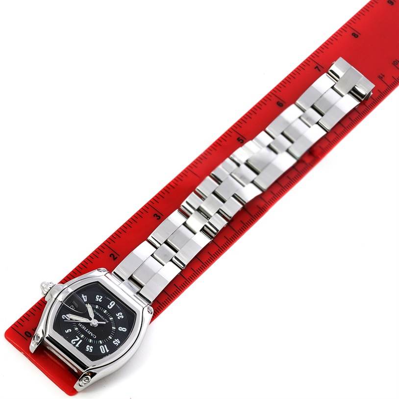 The Cartier Roadster W62004V3 Men's Stainless Steel Black Dial W62004V3 Men's Stainless Steel Black Dial watch is shown laid flat next to a red ruler, displaying its face and bracelet.
