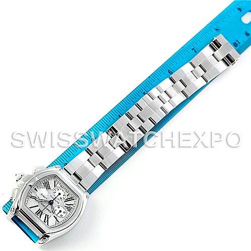 The Cartier Roadster W62019X6 Men's Stainless Steel Silver Dial W62019X6 Men's Stainless Steel Silver Dial watch is shown from an overhead view, displaying its face and full metal band laid alongside a blue ruler.