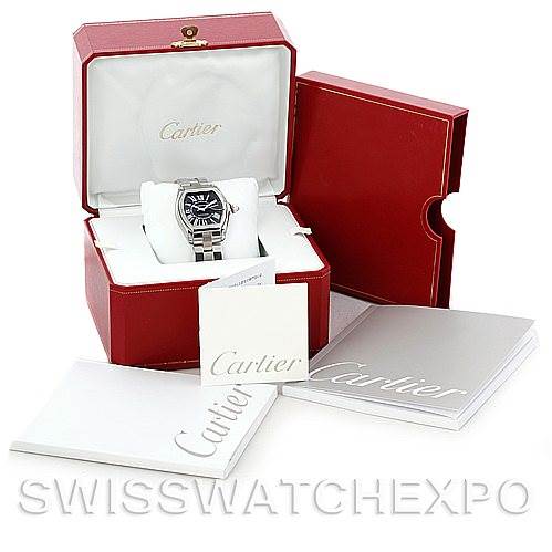 The image shows a Cartier Roadster W62041V3 Men's Stainless Steel Black Dial W62041V3 Men's Stainless Steel Black Dial watch in its open box, with accompanying booklets and additional packaging in the background.