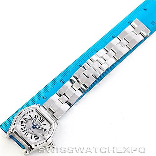 The image shows a top view of a Cartier Roadster W62025V3 Men's Stainless Steel Silver Dial W62025V3 Men's Stainless Steel Silver Dial watch next to a blue ruler, displaying its face and metal bracelet.