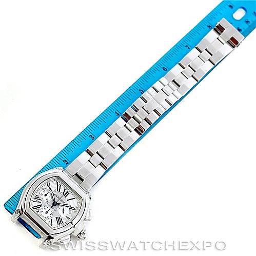 The image shows a Cartier Roadster W62019X6 Men's Stainless Steel Silver Dial W62019X6 Men's Stainless Steel Silver Dial watch laid flat next to a blue ruler with its face and stainless steel bracelet visible.