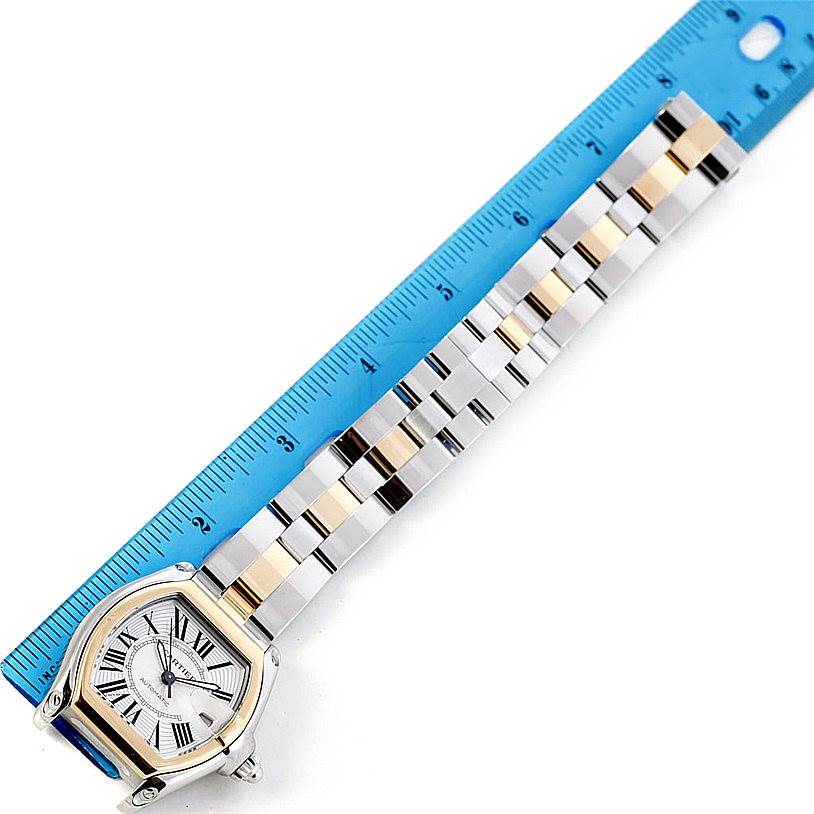 The image shows a Cartier Roadster W62031Y4 Men's Steel and Gold (two tone) Silver Dial W62031Y4 Men's Steel and Gold (two tone) Silver Dial watch displayed horizontally with a blue ruler along its bracelet for scale.