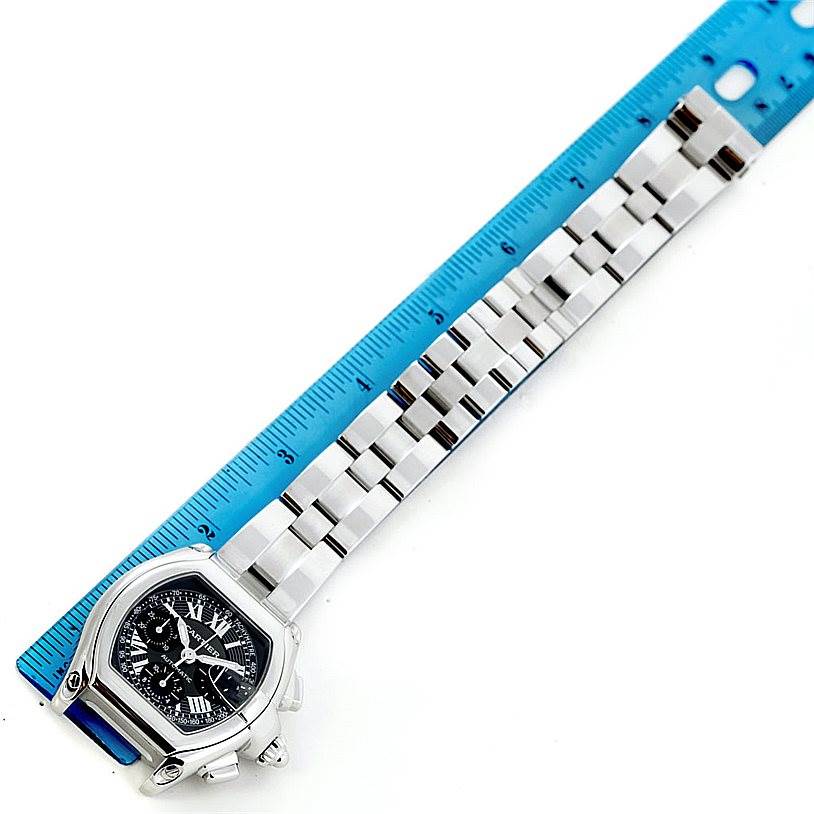 The Cartier Roadster W62007X6 Men's Stainless Steel Black Dial W62007X6 Men's Stainless Steel Black Dial watch is shown from a top-down angle alongside a blue ruler, displaying its face and metal bracelet.