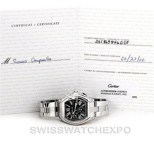 The image shows a Cartier Roadster W62020X6 Men's Stainless Steel Black Dial W62020X6 Men's Stainless Steel Black Dial watch at eye level, accompanied by its certificate and purchase documentation in the background.