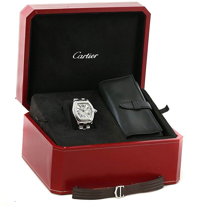 The Cartier Roadster W62032X6 Men's Stainless Steel Silver Dial W62032X6 Men's Stainless Steel Silver Dial watch is shown from a front angle inside an open red box, accompanied by a leather case and an additional strap.