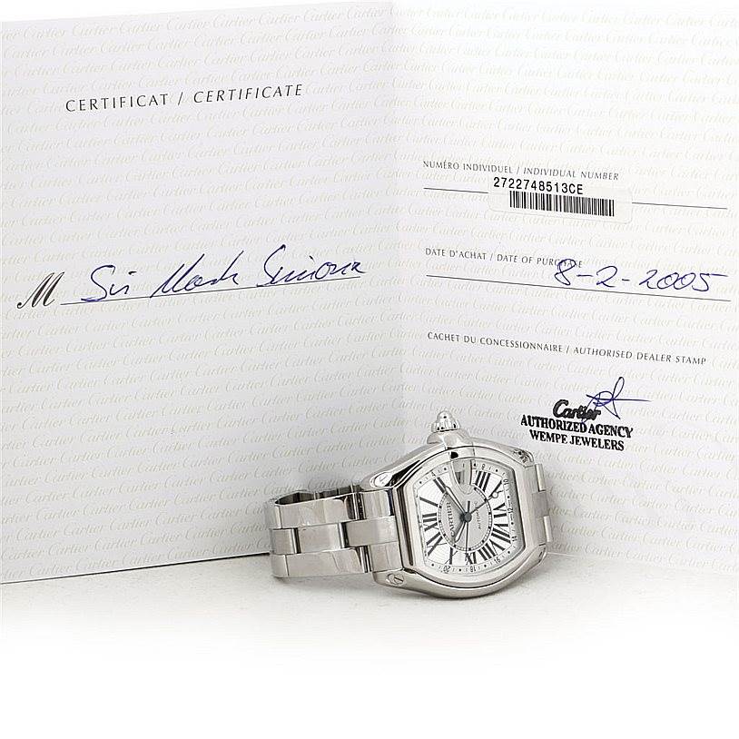 The image shows a Cartier Roadster W62032X6 Men
s Stainless Steel Silver Dial W62032X6 Men
s Stainless Steel Silver Dial watch with its certificate, resting on its side, displaying the face and part of the bracelet.