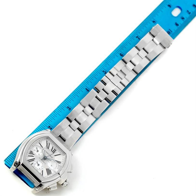 This image shows the Cartier Roadster W62019X6 Men's Stainless Steel Silver Dial W62019X6 Men's Stainless Steel Silver Dial watch laid flat with its face and stainless steel bracelet against a blue ruler for measurement.