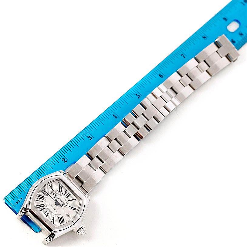 The image shows an overhead view of a Cartier Roadster W62025V3 Men's Stainless Steel Silver Dial W62025V3 Men's Stainless Steel Silver Dial watch next to a blue ruler, displaying the watch case and bracelet.