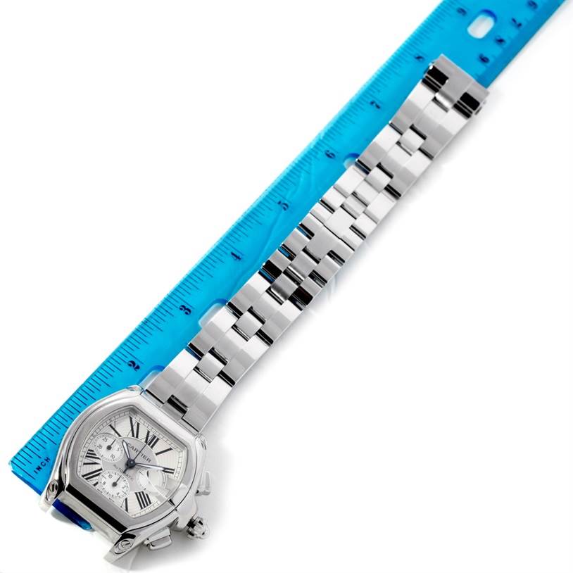 The Cartier Roadster W62019X6 Men's Stainless Steel Silver Dial W62019X6 Men's Stainless Steel Silver Dial watch is shown from a top-down angle, displaying the face and stainless steel bracelet next to a blue ruler.