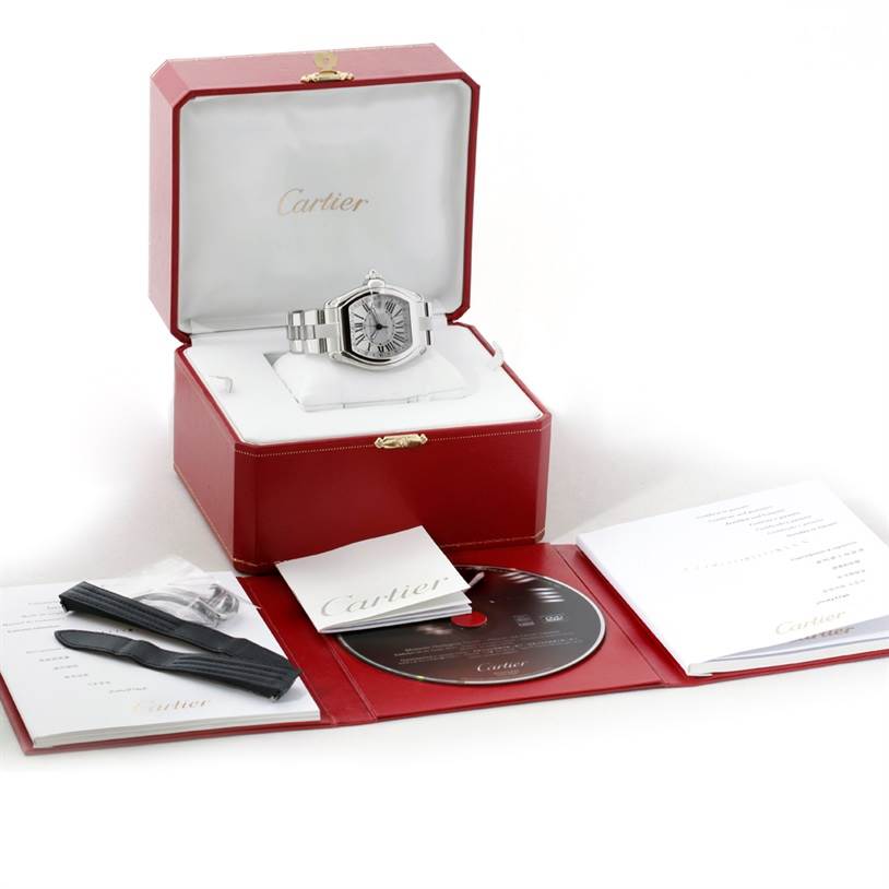The image shows a Cartier Roadster W62032X6 Men's Stainless Steel Silver Dial W62032X6 Men's Stainless Steel Silver Dial watch and accessories, including a red box, manuals, strap, and a CD, viewed from the front.
