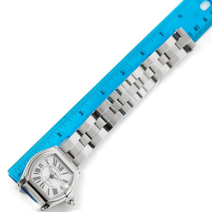 The Cartier Roadster W62025V3 Men's Stainless Steel Silver Dial W62025V3 Men's Stainless Steel Silver Dial watch is shown from a top-down angle, displaying its face and metal bracelet next to a blue ruler.