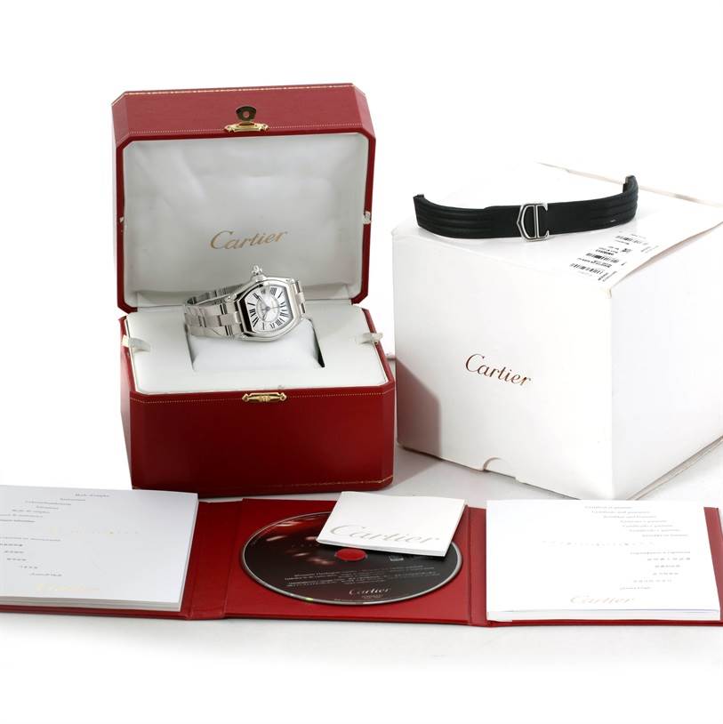 This image shows a Cartier Roadster W62025V3 Men's Stainless Steel Silver Dial W62025V3 Men's Stainless Steel Silver Dial model watch in its box, alongside its accessories including a manual, CD, and an additional strap.