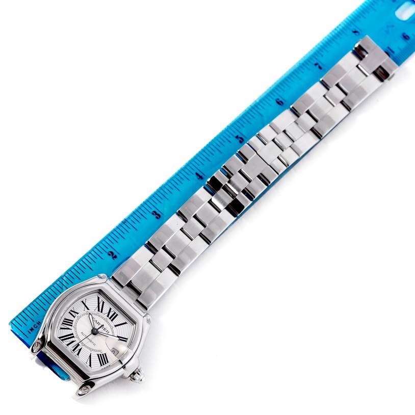 This image shows the Cartier Roadster W62025V3 Men's Stainless Steel Silver Dial W62025V3 Men's Stainless Steel Silver Dial watch lying flat with its face and bracelet visible, alongside a blue ruler for measurement.