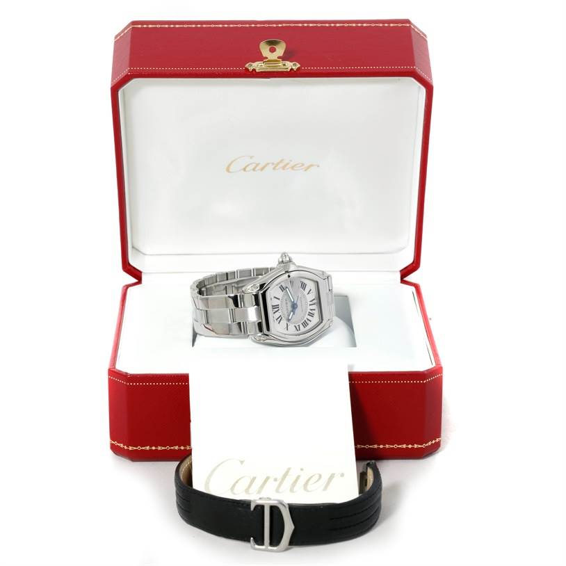 The image shows a Cartier Roadster W62000V3 Men's Stainless Steel Silver Dial W62000V3 Men's Stainless Steel Silver Dial watch with a metal bracelet, inside an open red Cartier box, and an additional black strap placed outside.