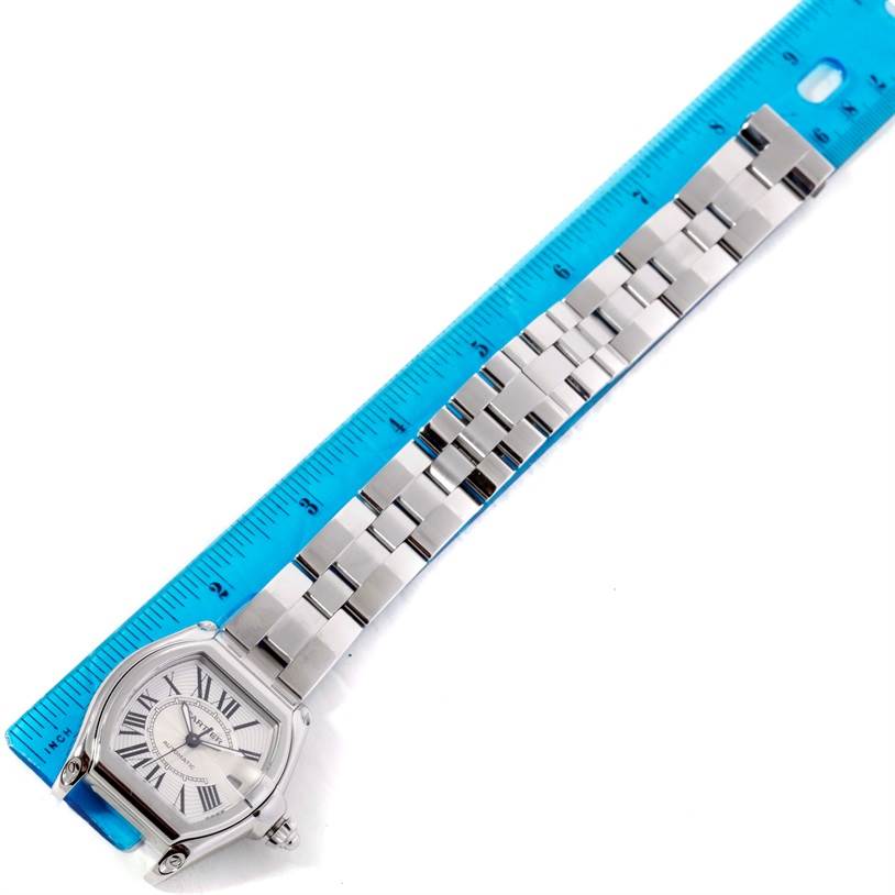 The image shows a Cartier Roadster W62025V3 Men's Stainless Steel Silver Dial W62025V3 Men's Stainless Steel Silver Dial watch positioned parallel to a blue ruler, displaying the face and full metal bracelet.