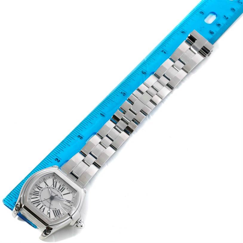 This image shows a Cartier Roadster W62032X6 Men's Stainless Steel Silver Dial W62032X6 Men's Stainless Steel Silver Dial watch with its stainless steel bracelet partially extended, alongside a blue ruler.