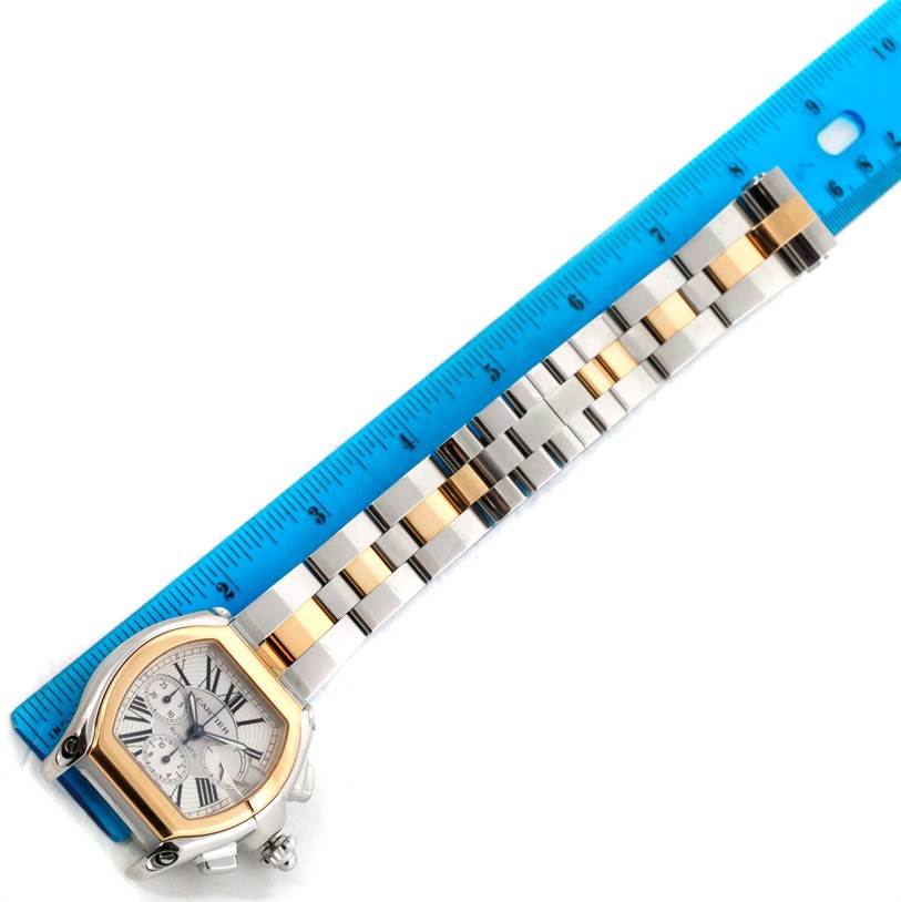 The Cartier Roadster W62027Z1 Men's Steel and Gold (two tone) Silver Dial W62027Z1 Men's Steel and Gold (two tone) Silver Dial watch is shown at an angle with its face and bracelet next to a blue ruler for measurement.