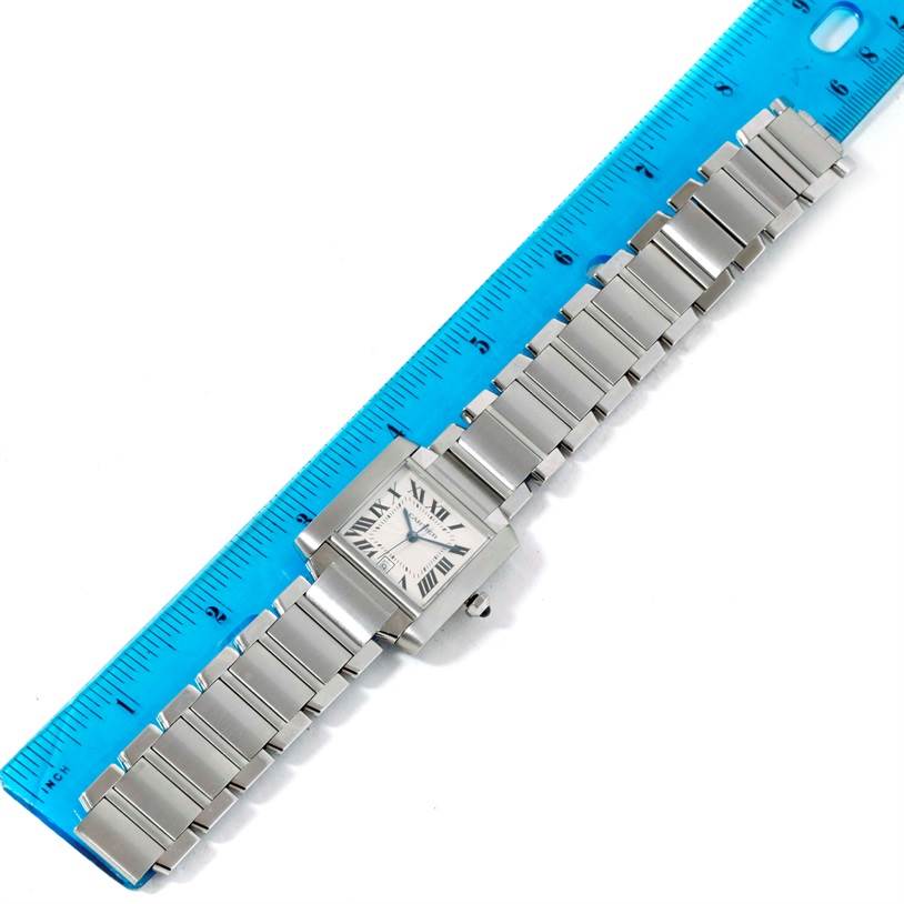 The Cartier Tank Française watch is shown from above, placed beside a blue ruler, displaying its square face and metallic bracelet.
