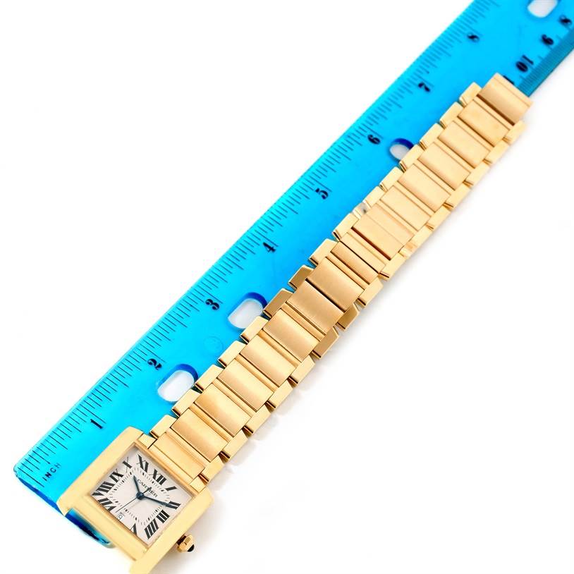 The Cartier Tank Francaise W50001R2 Men's Yellow Gold Silver Dial W50001R2 Men's Yellow Gold Silver Dial watch is shown from above, with its gold bracelet aligned against a blue ruler.