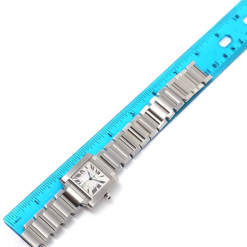 This image shows a Cartier Tank Française watch laid flat next to a blue ruler, highlighting its stainless steel bracelet and square face.