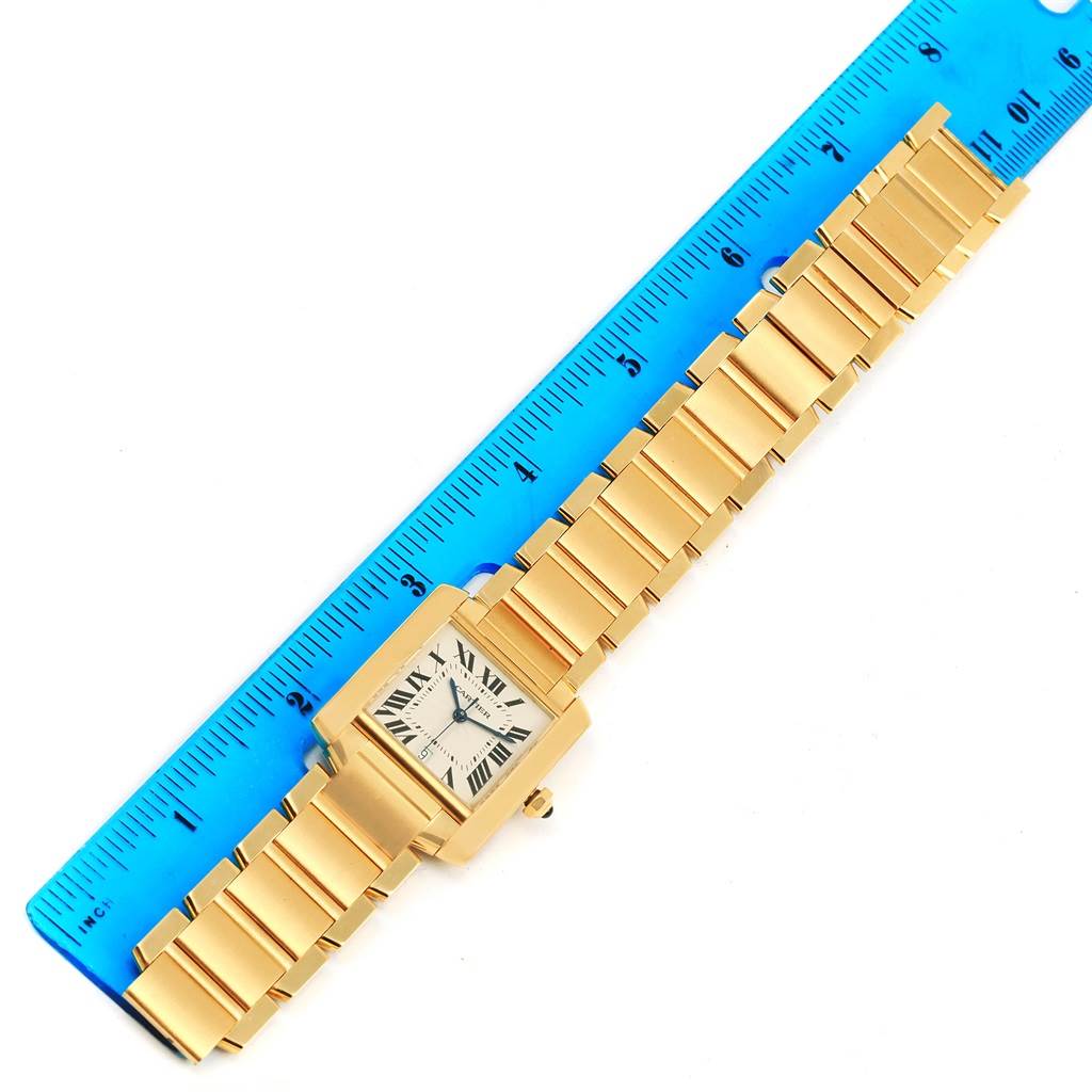The image shows a Cartier Tank Francaise W50001R2 Yellow Gold Silver Dial W50001R2 Yellow Gold Silver Dial watch placed next to a blue ruler from a top-down angle, displaying its face and band.