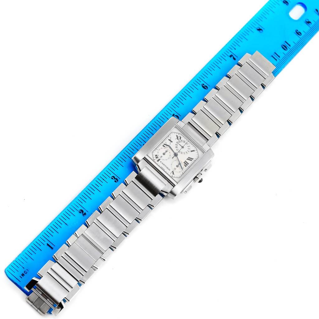 The Cartier Tank Française watch is shown face-up next to a blue ruler, displaying its dial and metal bracelet.