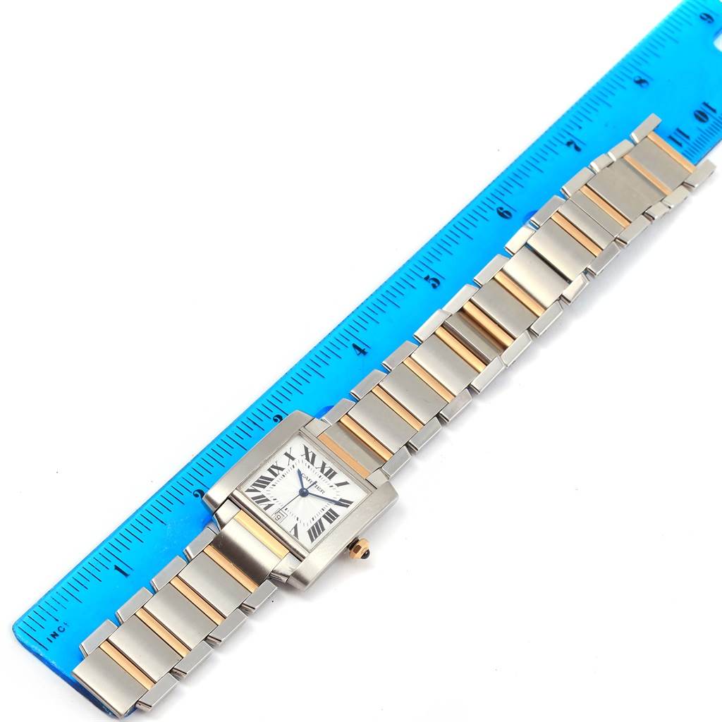 The image shows a Tank Française watch by Cartier laid flat next to a blue ruler, displaying the watch face and bracelet.