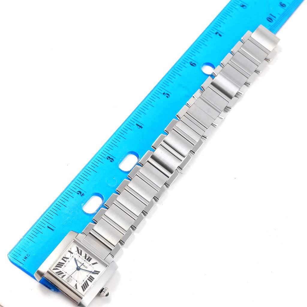 The Tank Francaise model by Cartier is shown from a top-down angle, displaying the watch face and the full metal bracelet next to a blue ruler.
