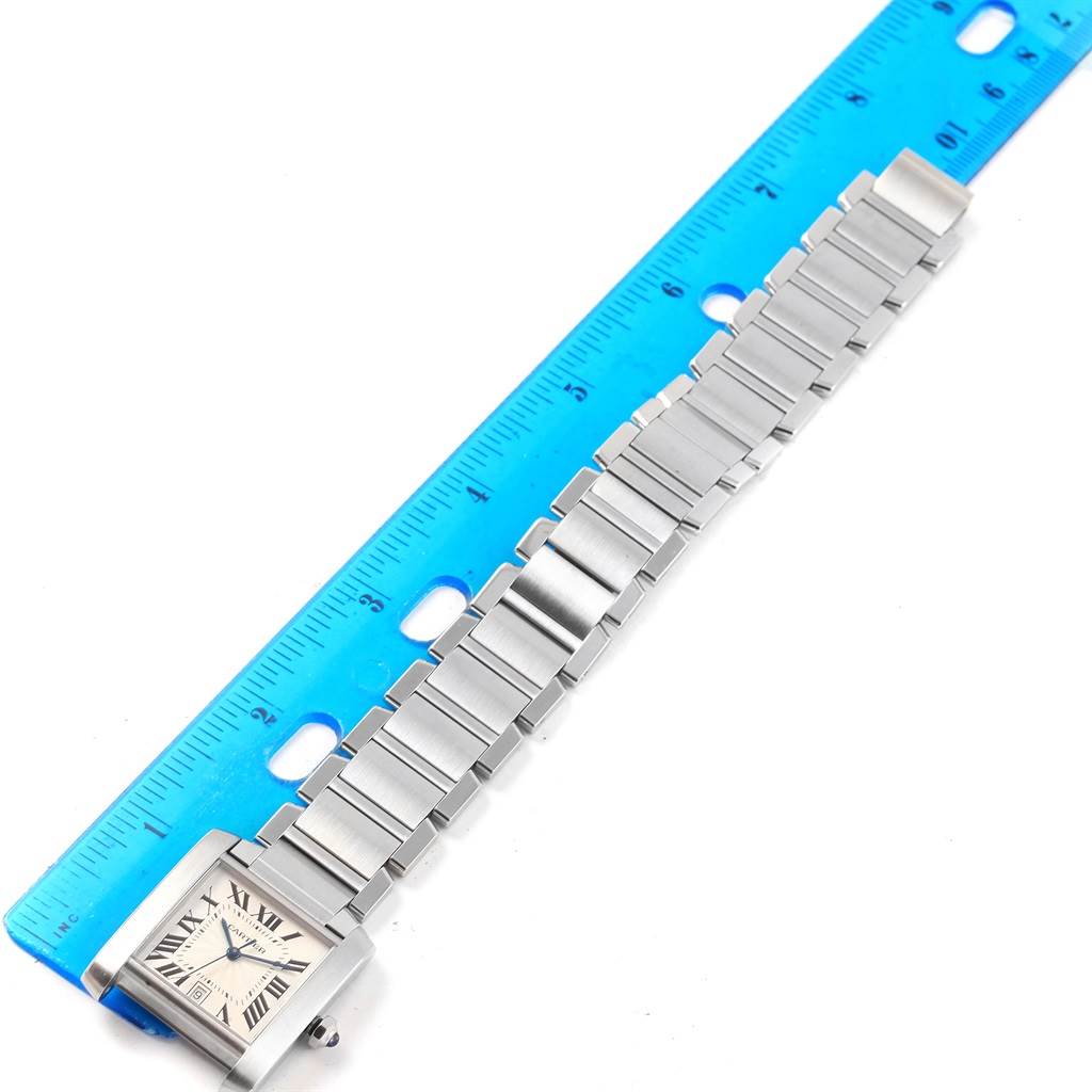 The Cartier Tank Francaise W51002Q3 Men
s Stainless Steel Silver Dial W51002Q3 Men
s Stainless Steel Silver Dial watch is shown lying flat next to a blue ruler, displaying its face and metallic strap.