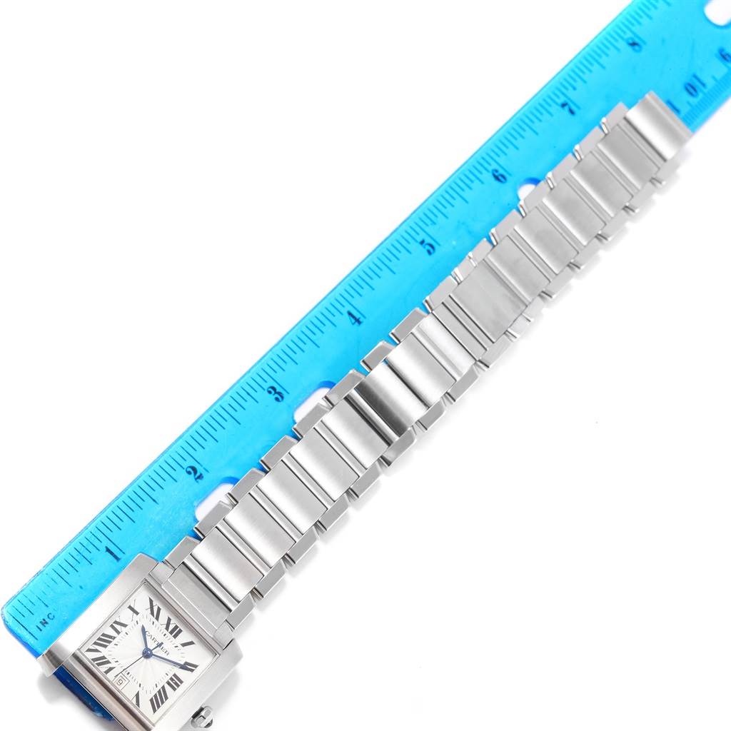 The image shows a top-down view of a Cartier Tank Francaise W51002Q3 Men's Stainless Steel Silver Dial W51002Q3 Men's Stainless Steel Silver Dial watch with a metal bracelet next to a blue ruler.
