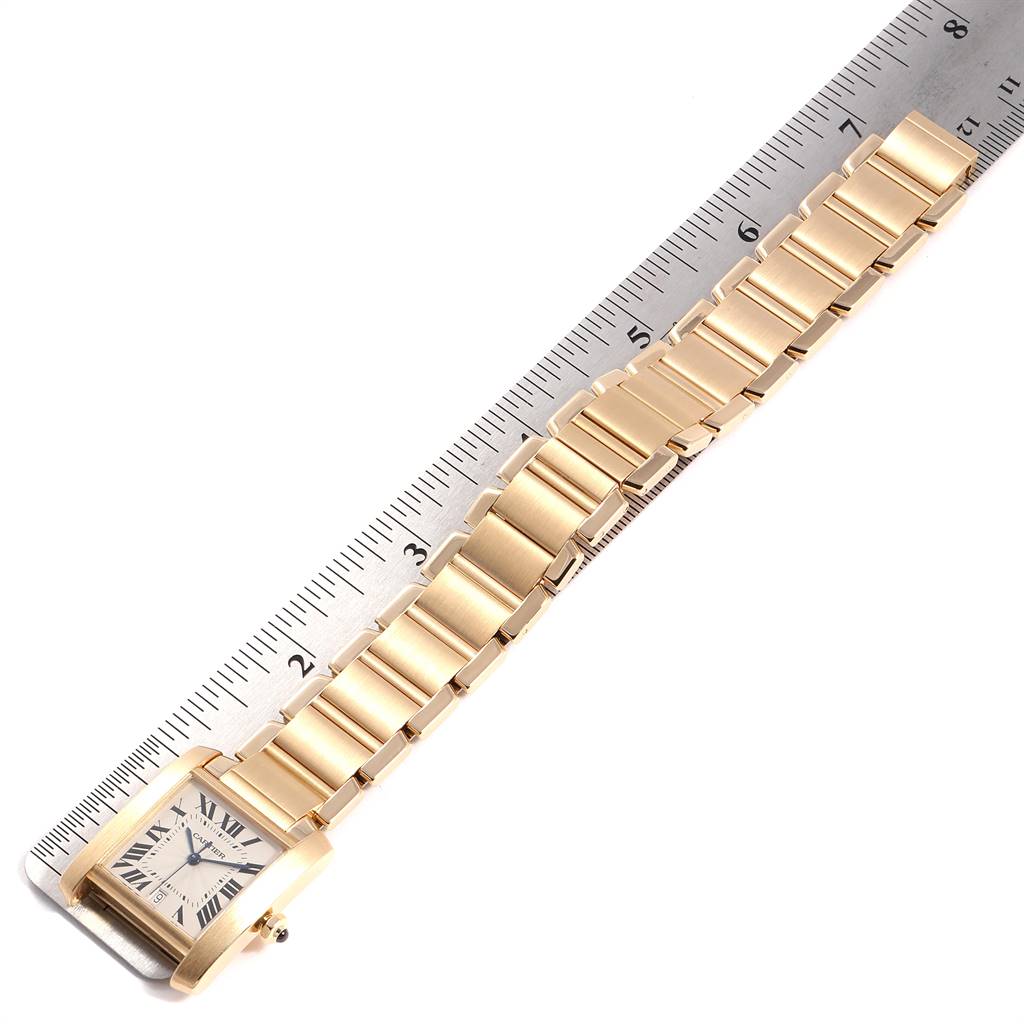 This image shows a Cartier Tank Francaise W50001R2 Yellow Gold Silver Dial W50001R2 Yellow Gold Silver Dial watch laid flat with its gold strap alongside a ruler, focusing on the bracelet and face.