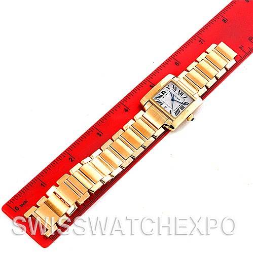 The image shows a Cartier Tank Francaise W50001R2 Men's Yellow Gold Silver Dial W50001R2 Men's Yellow Gold Silver Dial watch laid flat on a red ruler, highlighting its gold bracelet and square face.