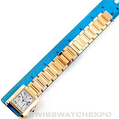 The image shows an overhead view of a Cartier Tank Francaise W50005R2 Men's Yellow Gold Silver Dial W50005R2 Men's Yellow Gold Silver Dial watch with a gold bracelet next to a blue ruler.