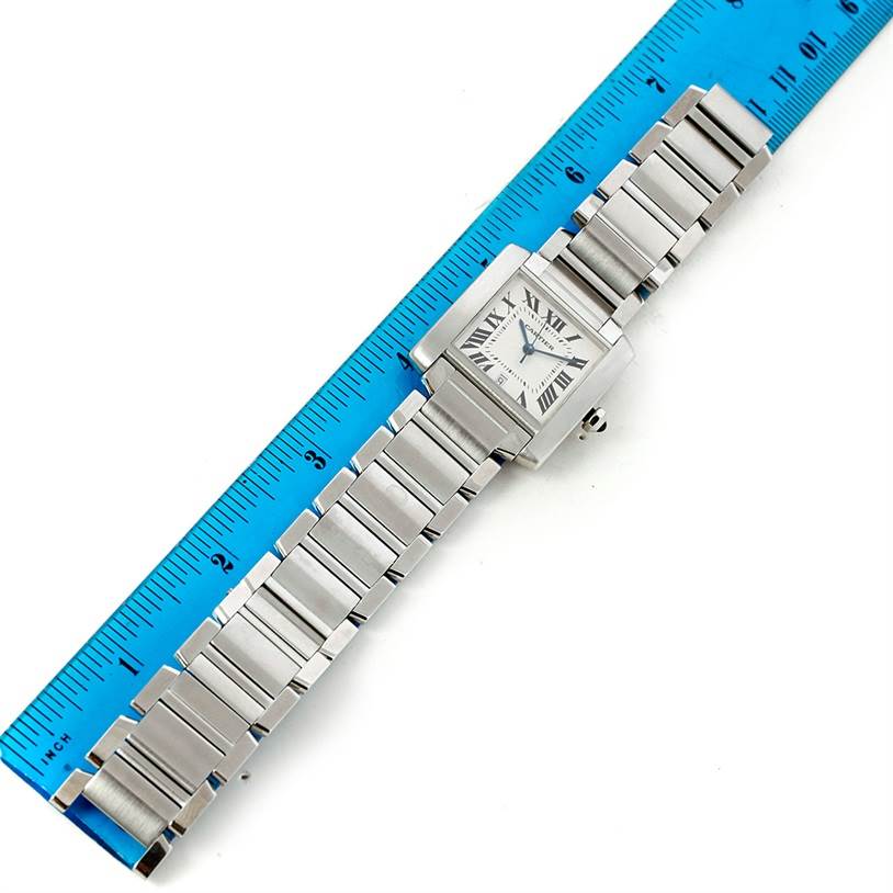 The image displays a top-down view of a Cartier Tank Française watch placed alongside a blue ruler.