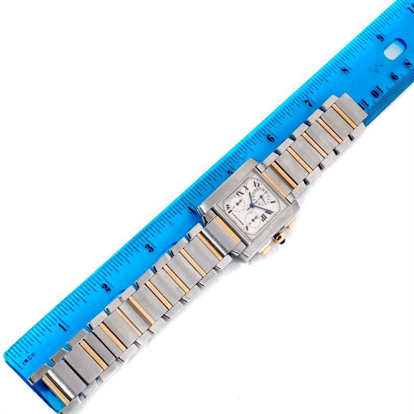 The Cartier Tank Française watch is shown from a top-down angle, displaying its face and metal bracelet alongside a blue ruler.