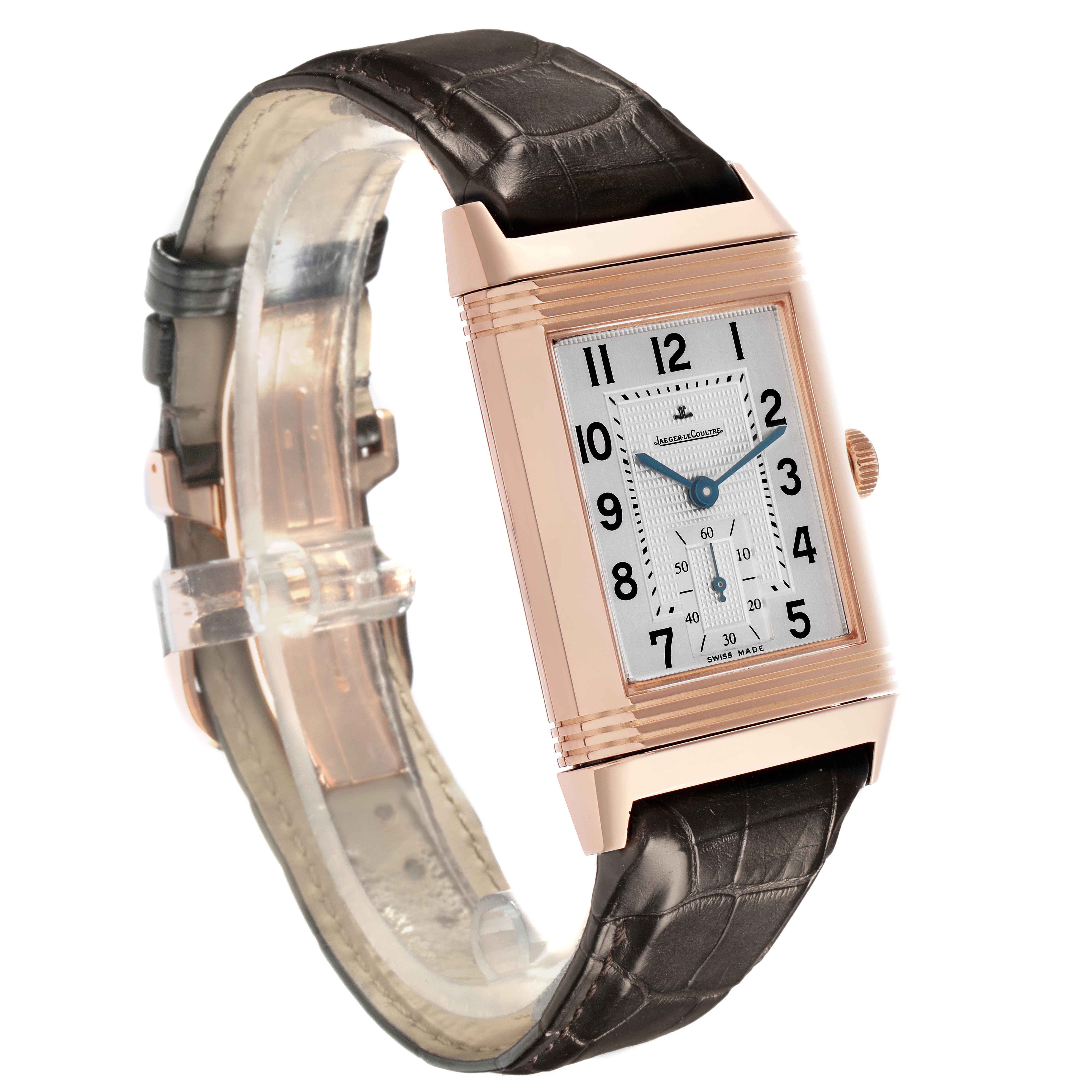 The Jaeger-LeCoultre Reverso watch is shown at a slight angle, highlighting its rectangular face, gold case, and alligator leather strap.